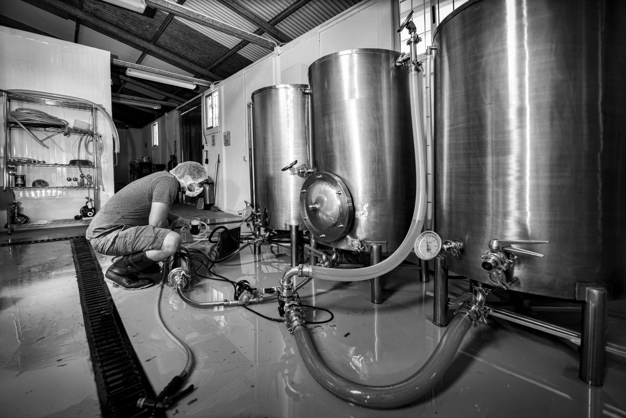 A brewer crouched by the pump, among the hoses and tanks