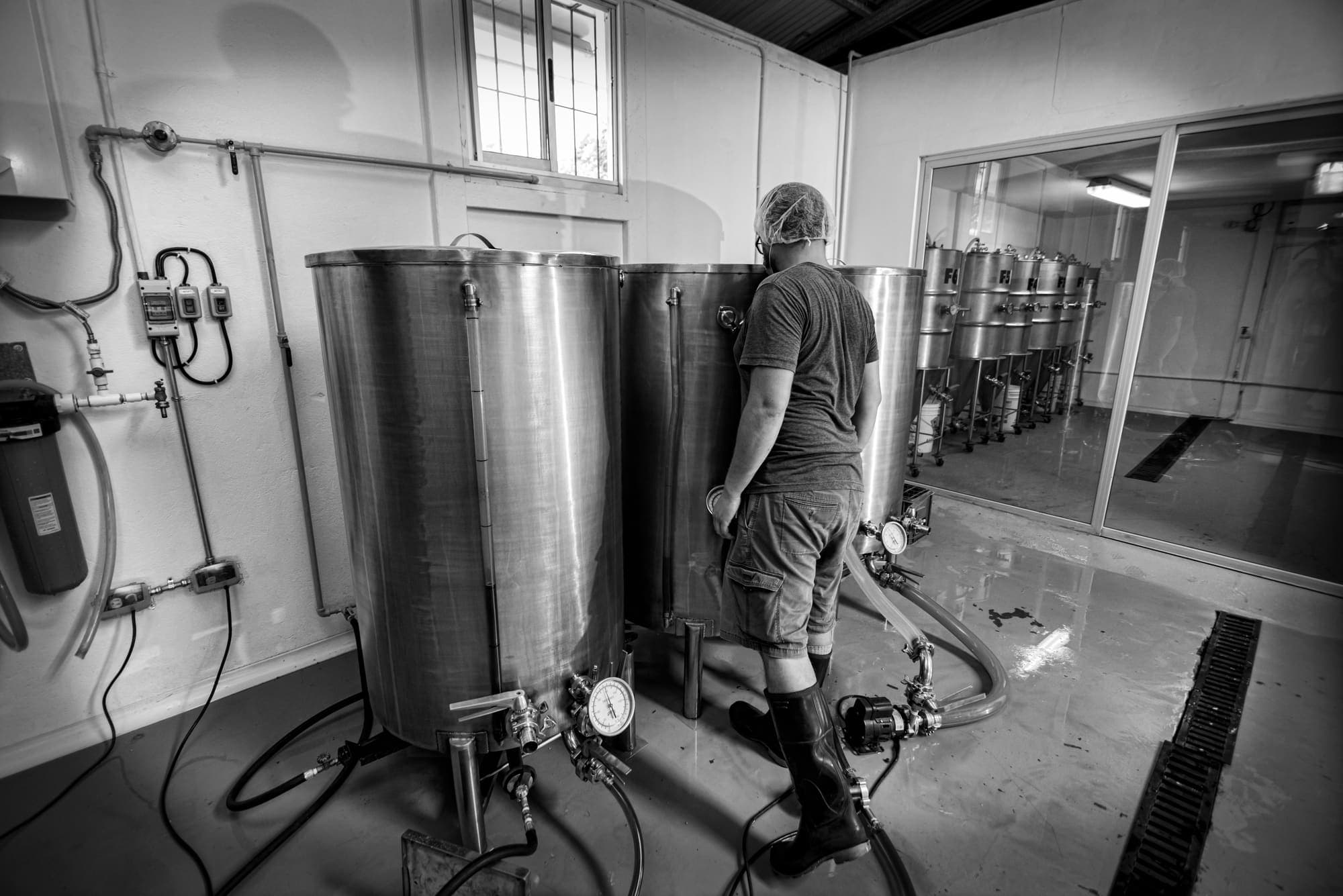 A brewer walking between the kettles, the fermenters behind the glass