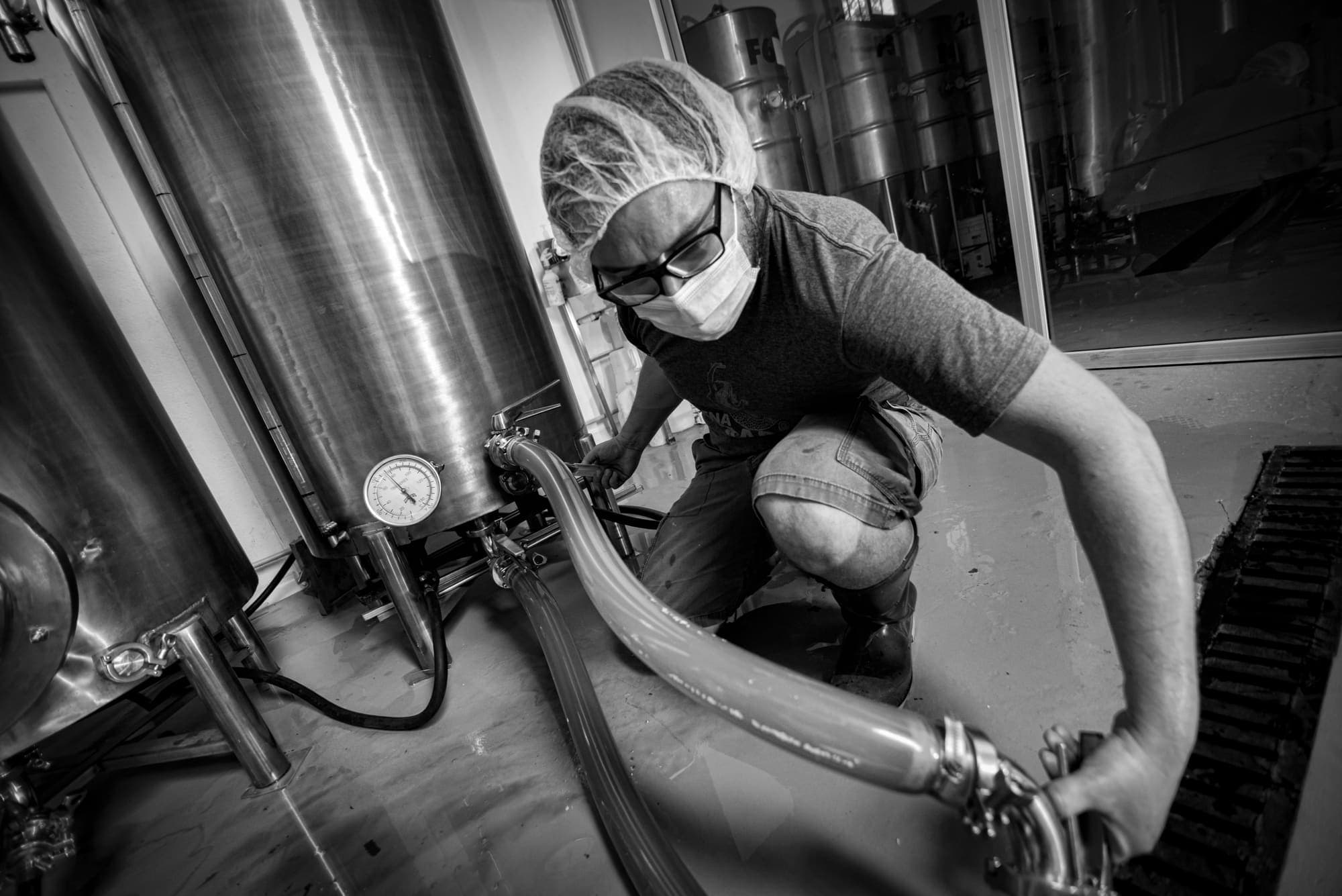 A brewer crouching to connect a hose to a tank valve