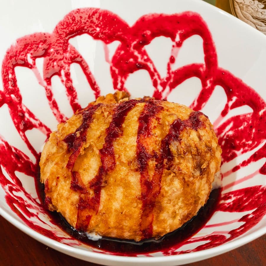 A ball of fried ice cream over a drawing of blackberry sauce on the plate