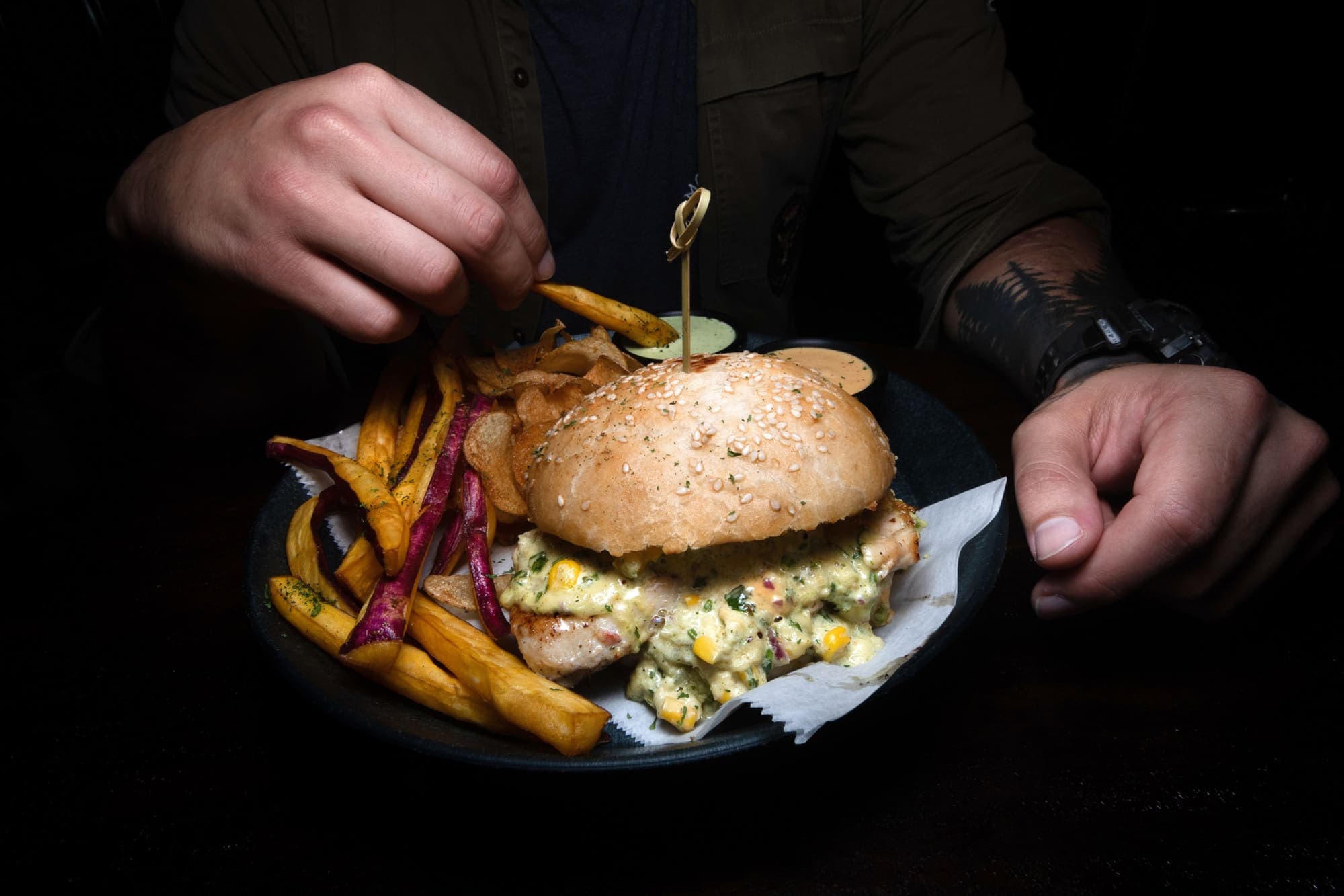A chicken breast burger with guacamole and creamed corn, with fries