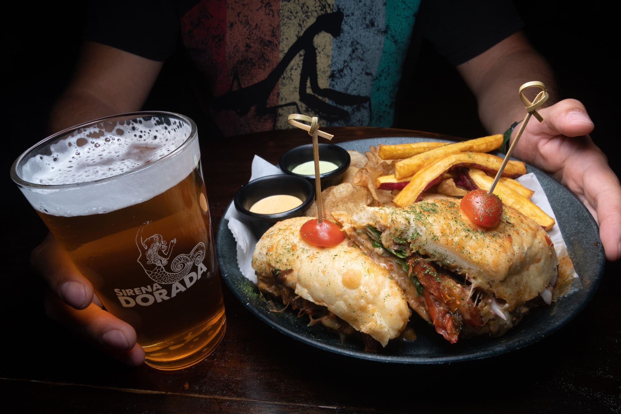 A sandwich with fries and a pint of golden beer beside it