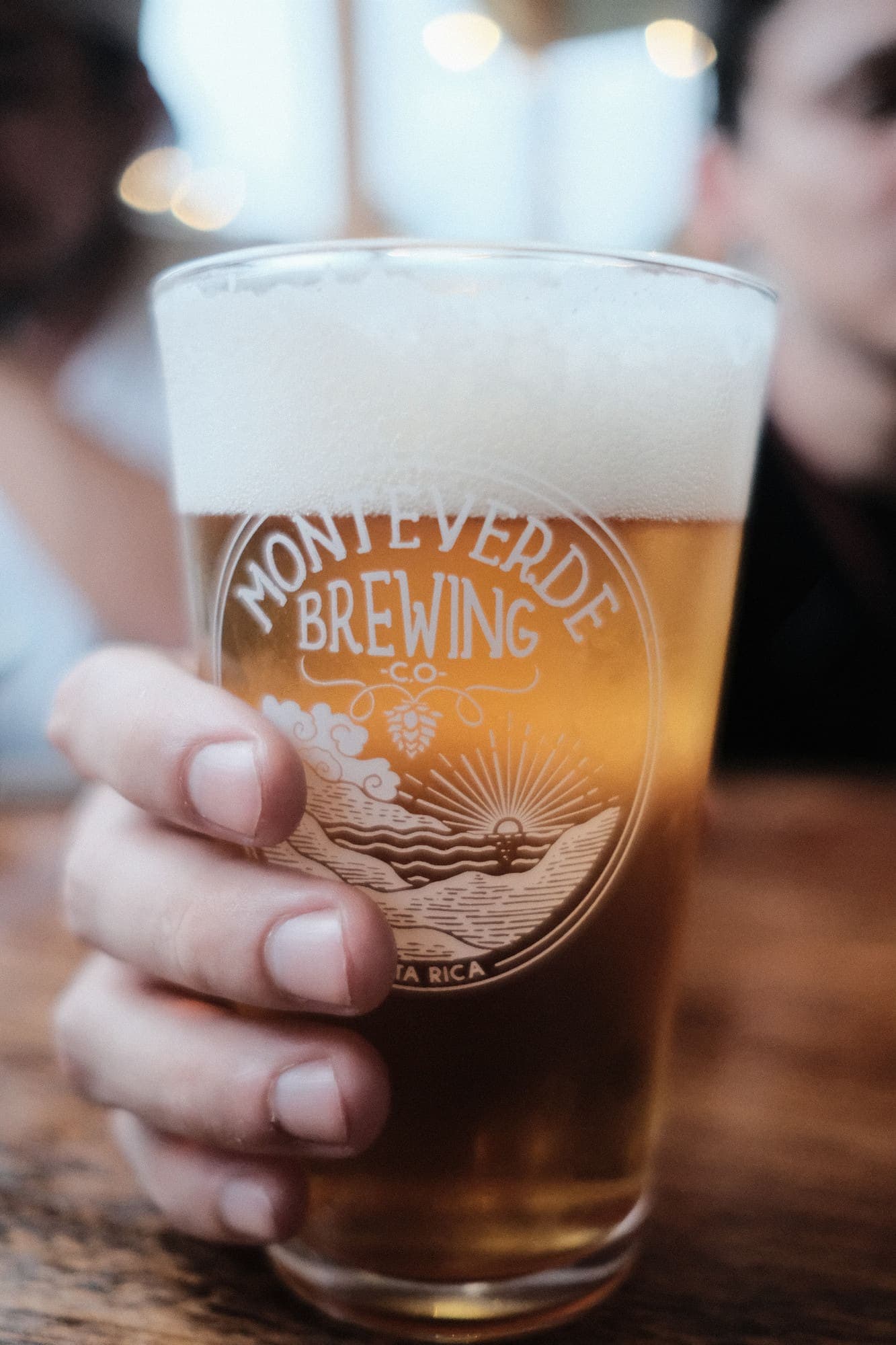 A pint of golden Monteverde Brewing Company beer held against the light in front of the forest