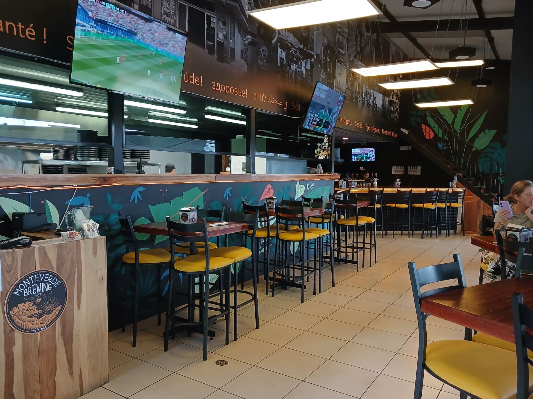 The floor of the Monteverde Brewing Company taproom in La Fortuna, with the bar and the leaf mural
